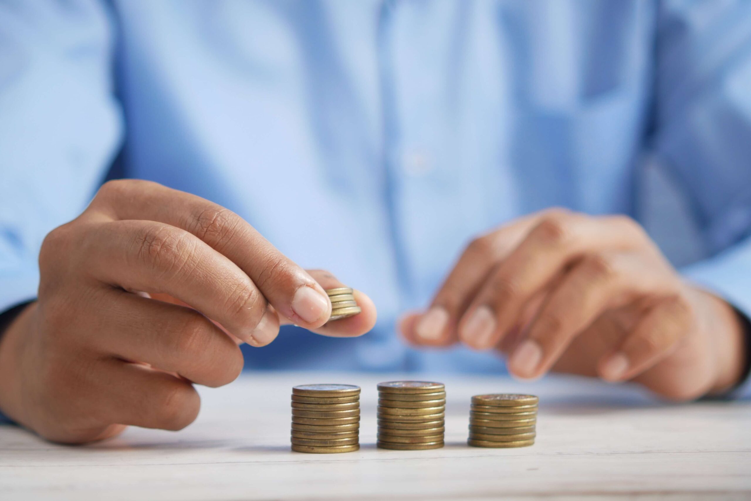 Man sorting coins into three piles in a blue button up shirt.